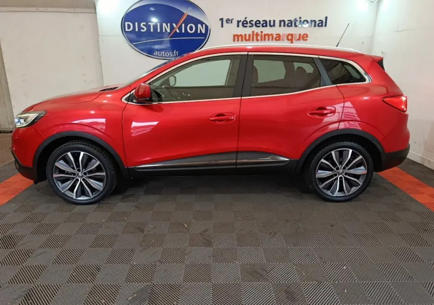 Profil côté gauche du Renault Kadjar rouge Intens Energy TCe 130 EDC avec jantes alliage et rails de toit chromés.