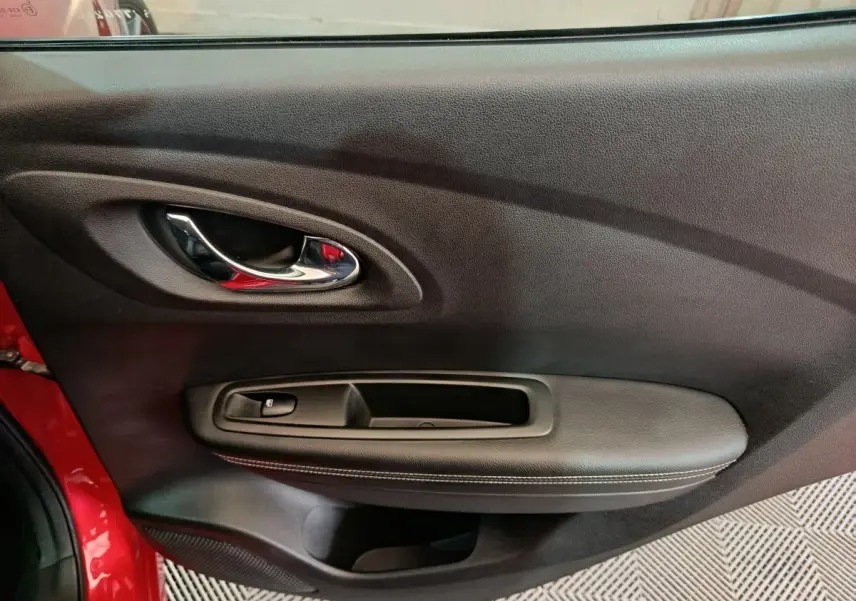Intérieur côté gauche de la porte rouge Renault Kadjar Intens, avec poignée chrome et commande de vitre noire.