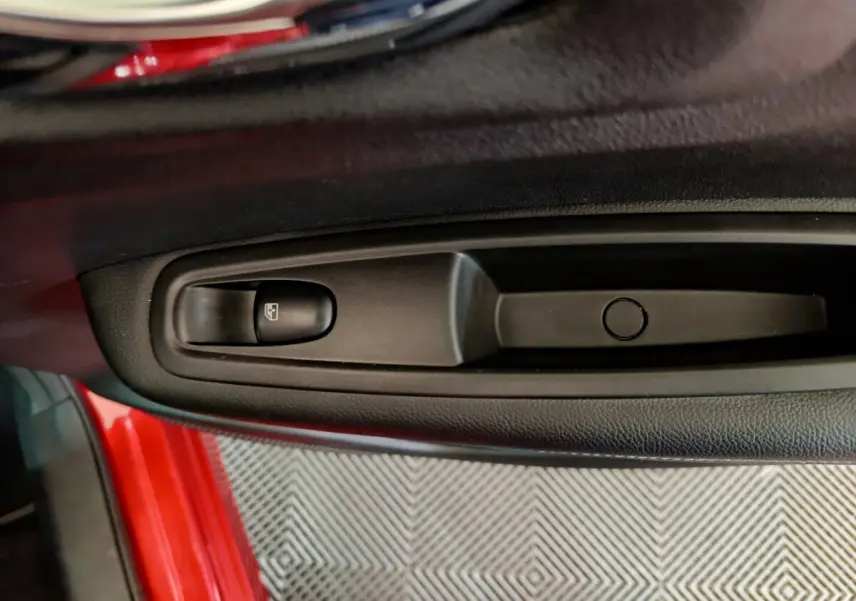 Gros plan sur la commande de lève-vitre côté conducteur d’un Renault Kadjar rouge visible à l’ouverture de la porte.