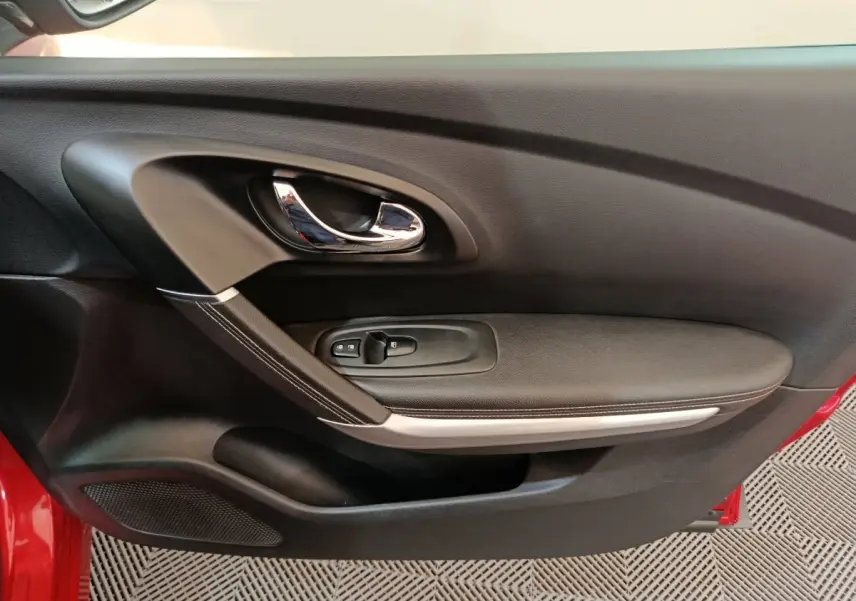Gros plan sur la porte côté gauche du Renault Kadjar rouge, montrant la poignée chromée et les commandes de fenêtre.