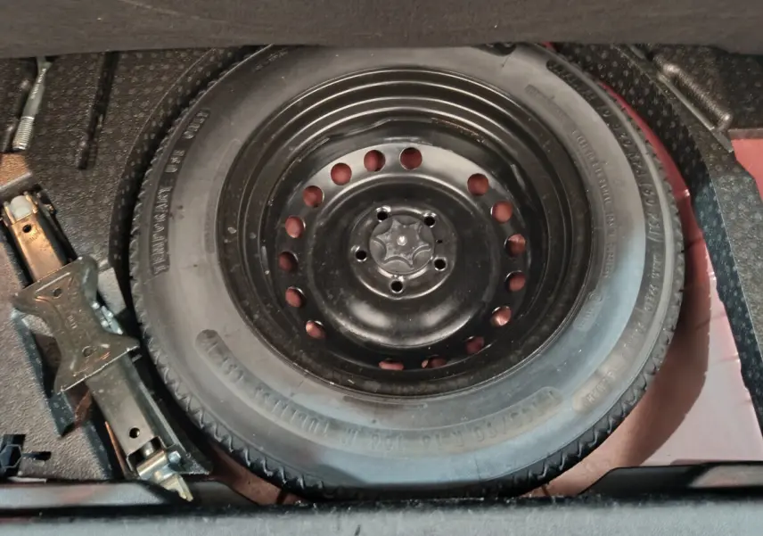 Gros plan sur la roue de secours noire et le cric dans le coffre du Renault Kadjar Intens rouge de 2017.