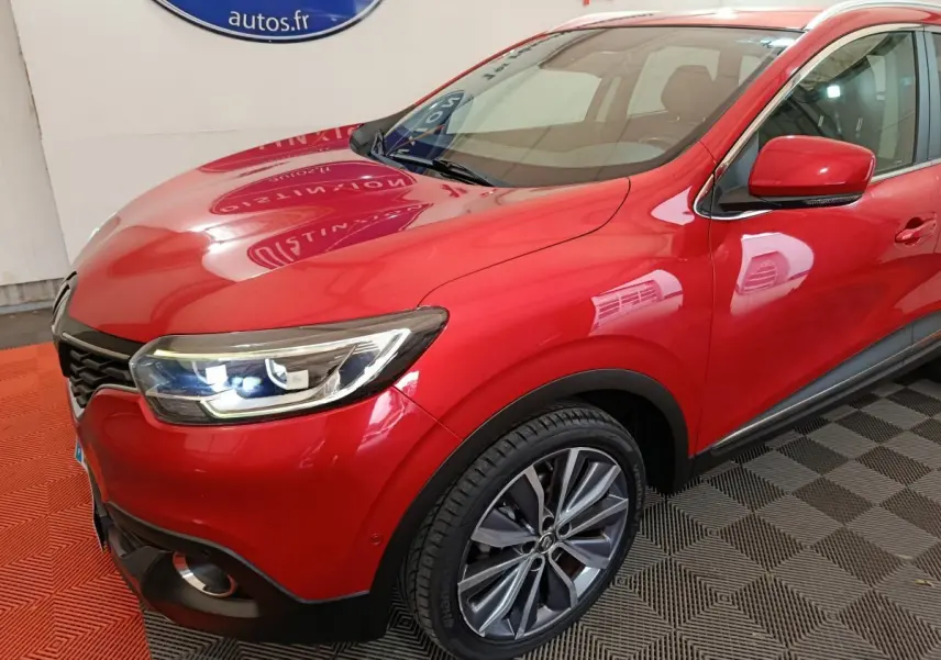 Vue 3/4 avant droite d'un Renault Kadjar Intens rouge avec phares LED allumés et jantes alliage visibles.