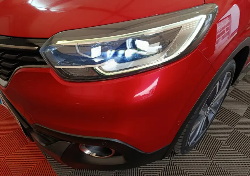 Gros plan sur le phare avant droit allumé d'un Renault Kadjar Intens rouge, avec partie de la calandre et roue visible.