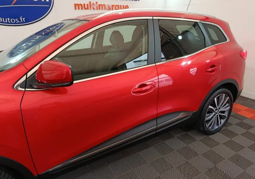 Profil côté gauche du Renault Kadjar rouge 2017 avec jantes alliage et rétroviseur assorti visible en intérieur showroom.