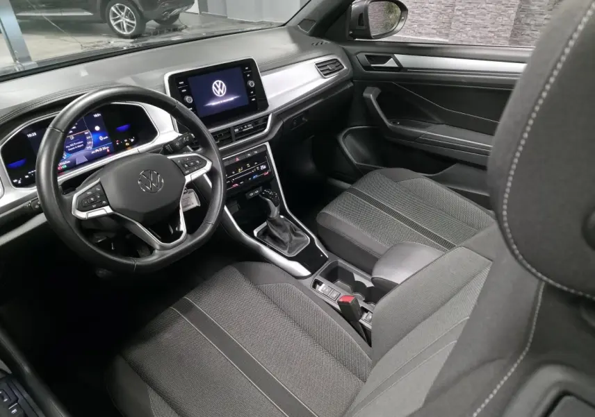 Intérieur avant du Volkswagen T-Roc 2024 avec sellerie tissu noire et tableau de bord numérique vu côté conducteur.