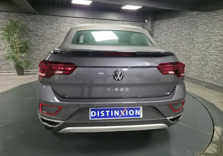 Vue arrière d'un Volkswagen T-Roc cabriolet gris métallisé avec capote textile grise dans un showroom.
