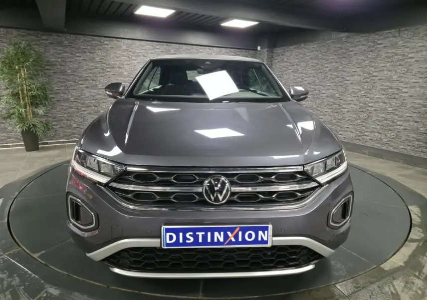 Vue frontale d'un Volkswagen T-Roc Cabriolet gris métallisé 2024 avec calandre chromée et plaque Distinxion.