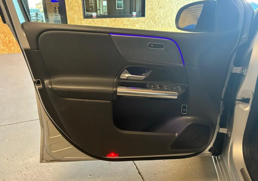 Vue intérieure de la porte avant gauche gris foncé d'une Mercedes Classe B 200D Progressive Line avec éclairage d'ambiance bleu.