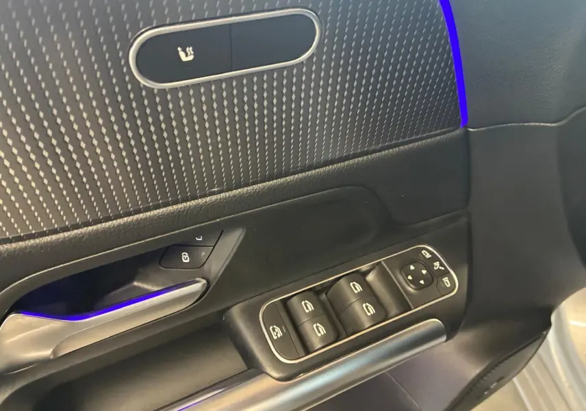 Détail de la porte côté conducteur d'une Mercedes Classe B 200D gris, avec commandes électriques et éclairage d'ambiance bleu.