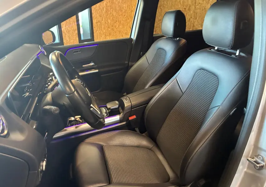 Vue intérieure côté conducteur de la Mercedes Classe B 200D gris, sièges en cuir noir avec éclairage d'ambiance violet.
