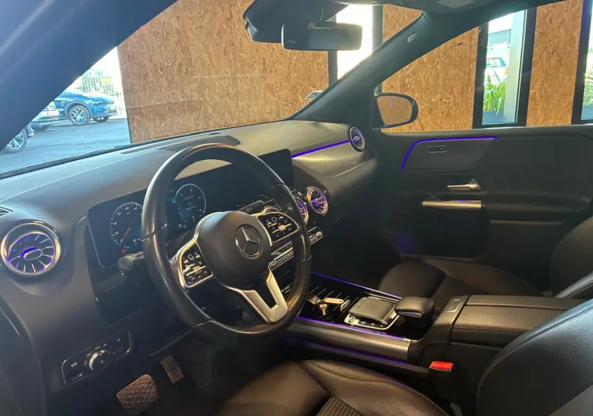 Intérieur avant droit d'une Mercedes Classe B 200D gris, volant multifonctions et éclairage d'ambiance violet visible.