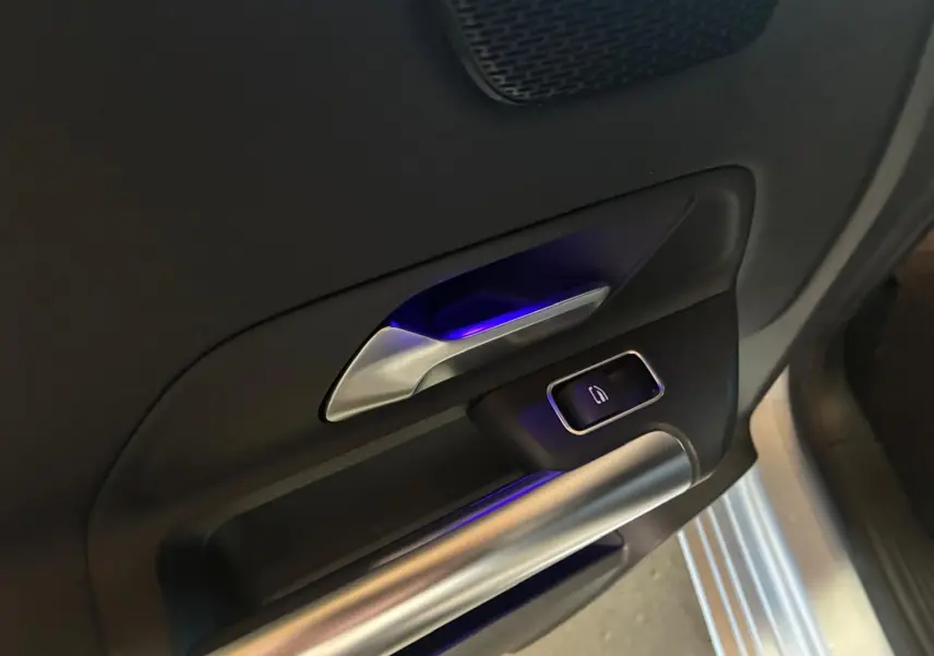 Gros plan sur la poignée intérieure côté gauche d’une Mercedes Classe B 200D gris, avec éclairage bleu subtil.