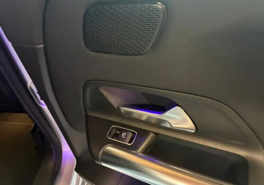 Gros plan sur la poignée intérieure côté gauche de la porte d’une Mercedes Classe B 200D gris, avec bouton de commande.