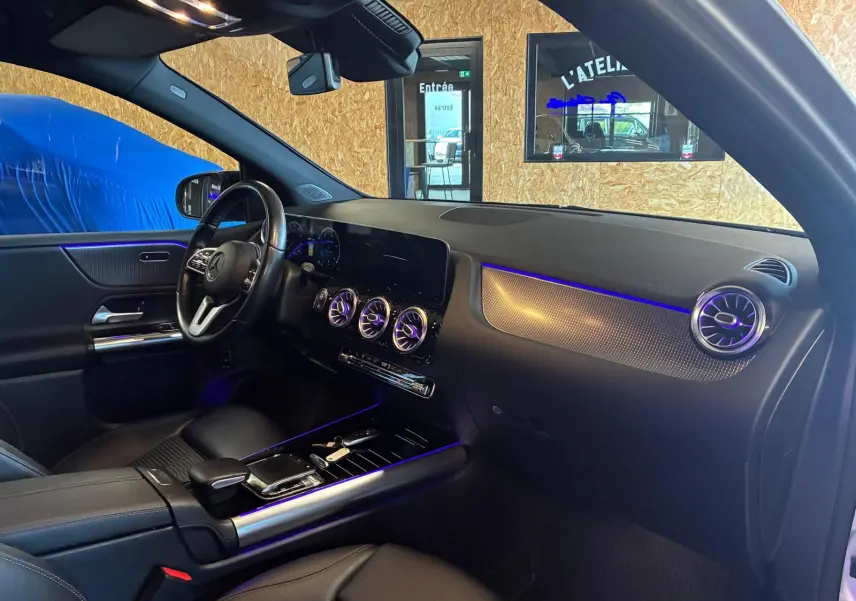 Vue intérieure côté conducteur de la Mercedes Classe B 200D gris, avec éclairage d’ambiance bleu et tableau de bord moderne.