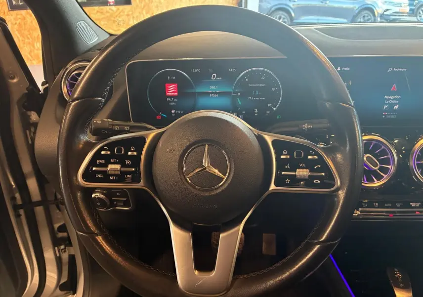 Vue intérieure centrée sur le volant cuir noir de la Mercedes Classe B 200D 2019 avec tableau de bord numérique et écran tactile.