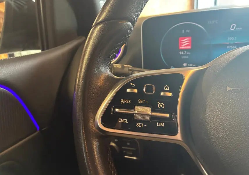 Gros plan sur le volant cuir noir côté gauche d'une Mercedes Classe B 200D gris, avec commandes intégrées et tableau de bord digital.