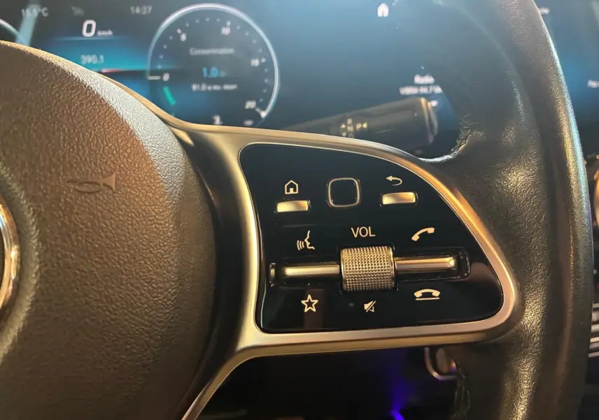 Gros plan sur la commande de volume au volant cuir noir d'une Mercedes Classe B 200D gris, avec tableau de bord numérique.