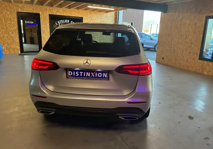 Vue arrière d'une Mercedes Classe B 200D Progressive Line gris, feux arrière allumés dans un garage.