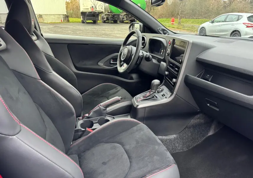 Vue intérieure côté conducteur de la Toyota Yaris GR avec sièges sport noirs et surpiqûres rouges visibles.