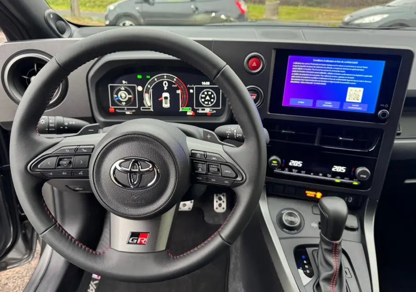 Vue intérieure centrée sur le volant Toyota Yaris GR avec surpiqûres rouges et écran tactile du tableau de bord.