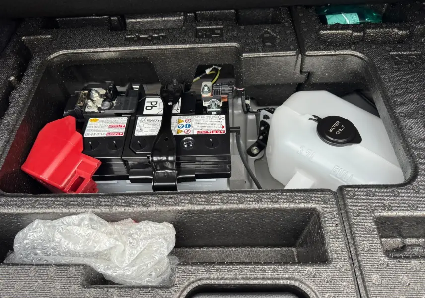 Gros plan sur la batterie et le réservoir d'eau sous le coffre d'une Toyota Yaris GR Pack Techno, compartiment en mousse noire.