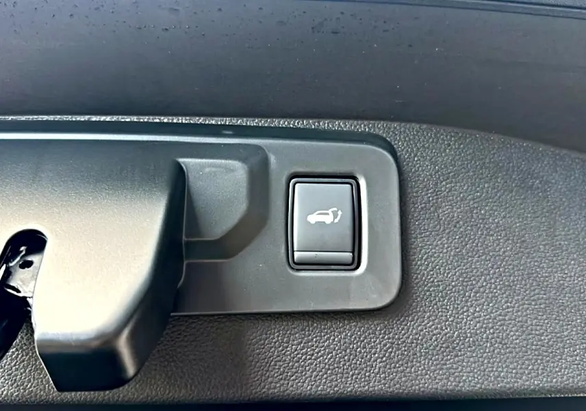 Gros plan sur le bouton d'ouverture électrique du coffre, intérieur noir texturé du Renault Austral bleu outremer.