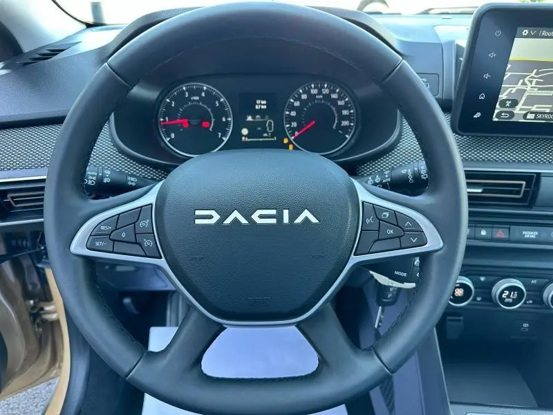 Vue rapprochée du volant DACIA noir avec commandes intégrées et tableau de bord numérique d'une Sandero beige Safari 2025.