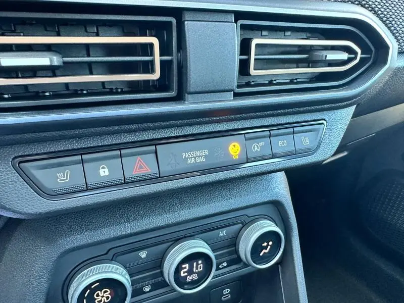 Vue rapprochée du tableau de bord noir du Dacia Sandero beige Safari 2025, mettant en valeur les commandes de climatisation et sécurité.