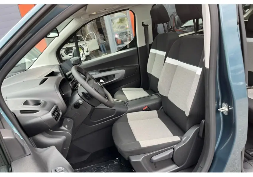 Vue intérieure côté conducteur du Citroën Berlingo bleu 2025, sièges bicolores gris et noir, tableau de bord moderne.