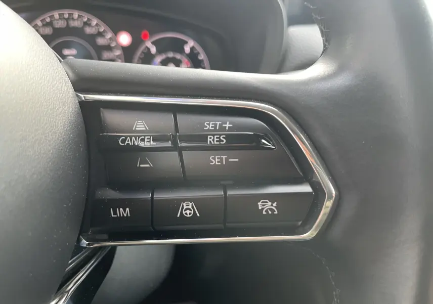 Gros plan sur les commandes de régulateur de vitesse au volant du Mazda CX-60 2023 blanc nacré, intérieur gris noir.