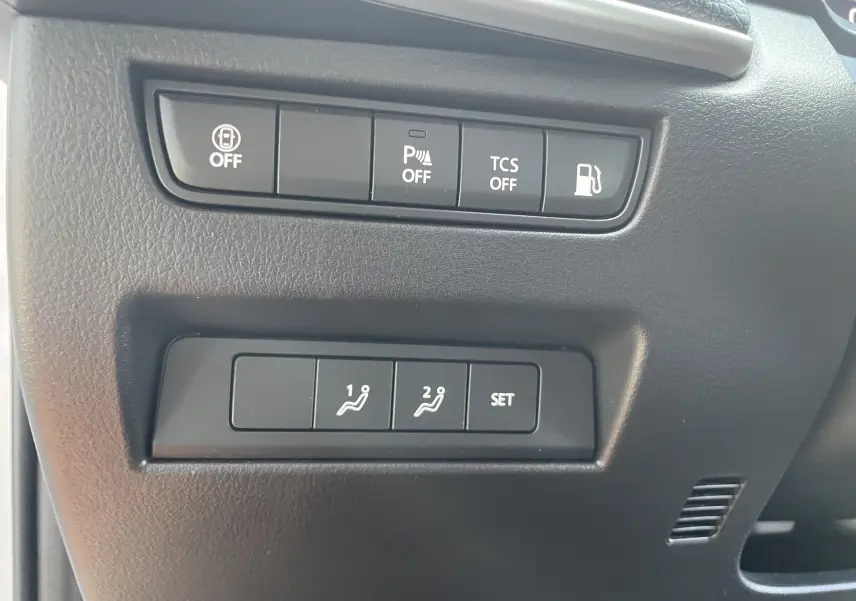 Gros plan sur les boutons de réglage des sièges et commandes d'assistance du tableau de bord d'un Mazda CX-60 blanc nacré 2023.