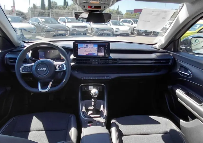 Vue intérieure avant du Jeep Avenger 2025, tableau de bord noir avec écran tactile et levier de vitesse manuel visible.