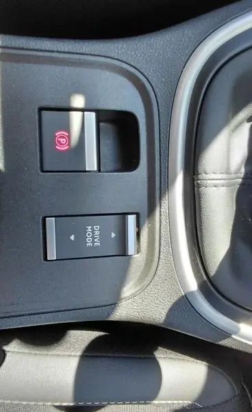 Gros plan sur la console centrale du Jeep Avenger blanc 2025, montrant les boutons frein électronique et mode de conduite.