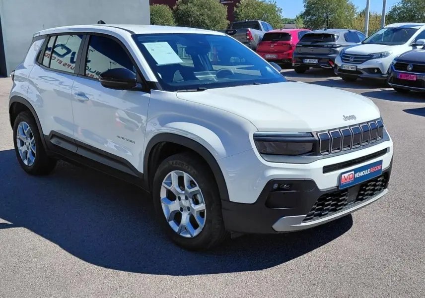 Jeep Avenger blanc en 3/4 avant droit, avec calandre distinctive et jantes alliage, stationné en extérieur.