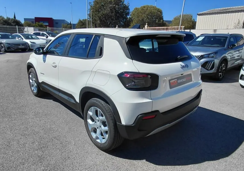 Jeep Avenger blanc en 3/4 arrière droit, avec feux arrière noirs et jantes argentées, stationné en extérieur.