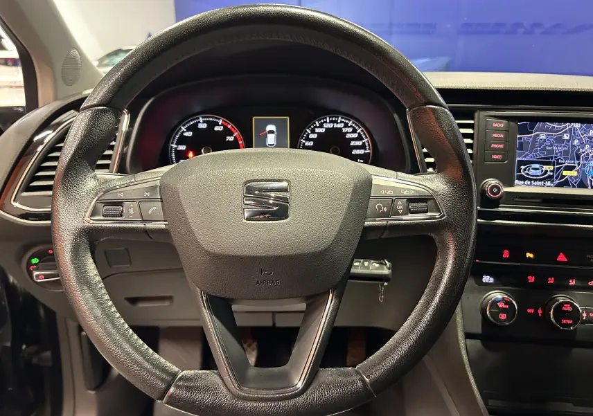 Vue intérieure centrée sur le volant en cuir noir d'une SEAT Leon 2014 avec tableau de bord et écran GPS allumé.