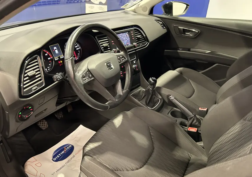 Vue intérieure côté conducteur de la SEAT Leon noire, montrant le volant cuir, la boîte manuelle et l’écran GPS intégré.