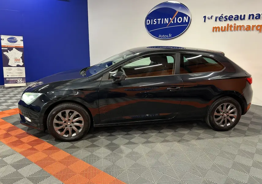 Vue de profil côté gauche d'une SEAT Leon noire 3 portes, dans un showroom avec sol gris et orange.