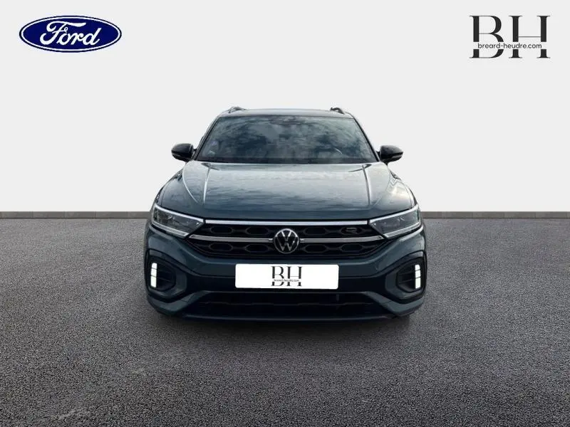 Volkswagen T-Roc 1.5 TSI R-Line bleu pétrole métallisé vue de face avec calandre noire et feux LED allumés.