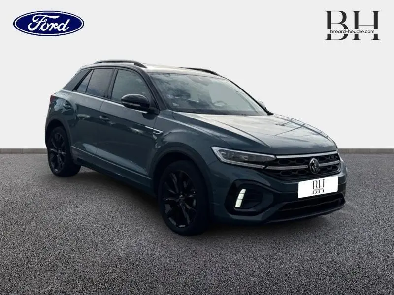 Volkswagen T-Roc 1.5 TSI R-Line bleu pétrole métallisé, vue 3/4 avant droit avec jantes noires et barres de toit.