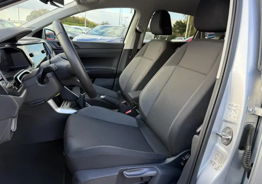 Intérieur avant droit d'une Volkswagen Polo 2025 gris Reflet Argent, sièges tissu noir et tableau de bord moderne.