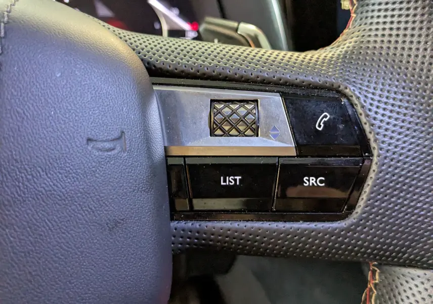 Gros plan sur les commandes gauche du volant perforé noir du DS7 2025, avec molette et boutons LIST et SRC.