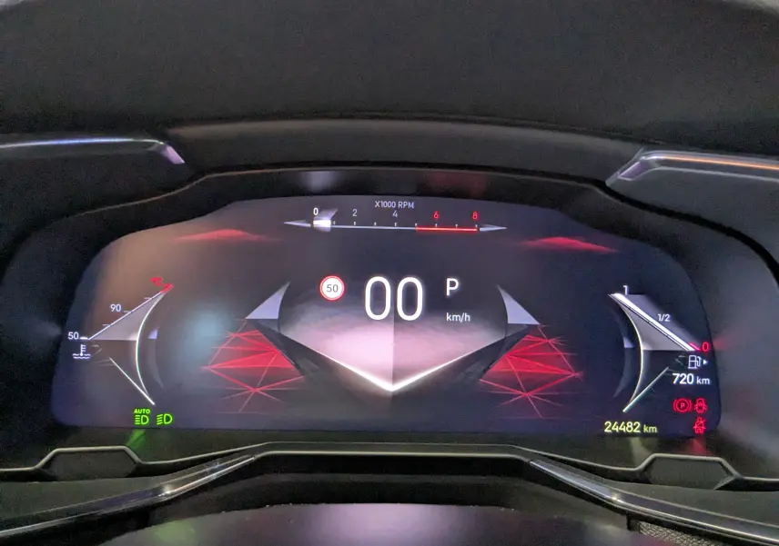 Vue rapprochée du tableau de bord numérique du DS7 gris laqué, affichant la vitesse à 0 km/h et divers indicateurs lumineux.