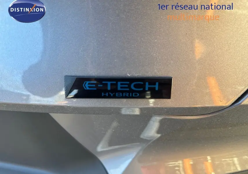 Gros plan sur l'insigne E-TECH Hybrid sur la carrosserie gris cassiopée métal d'une Renault Symbioz 2024.