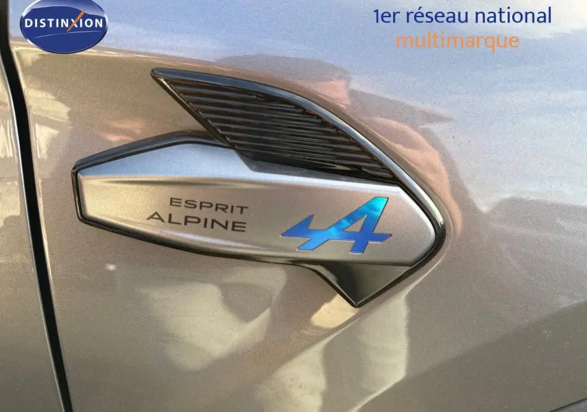 Gros plan sur l'emblème Esprit Alpine bleu sur la carrosserie gris cassiopée métal d'une Renault Symbioz 2024.