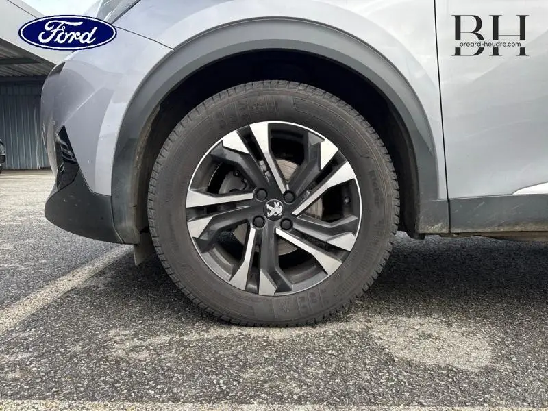 Gros plan sur la roue avant gauche d'un Peugeot 2008 gris Artense avec jante alu au design moderne.