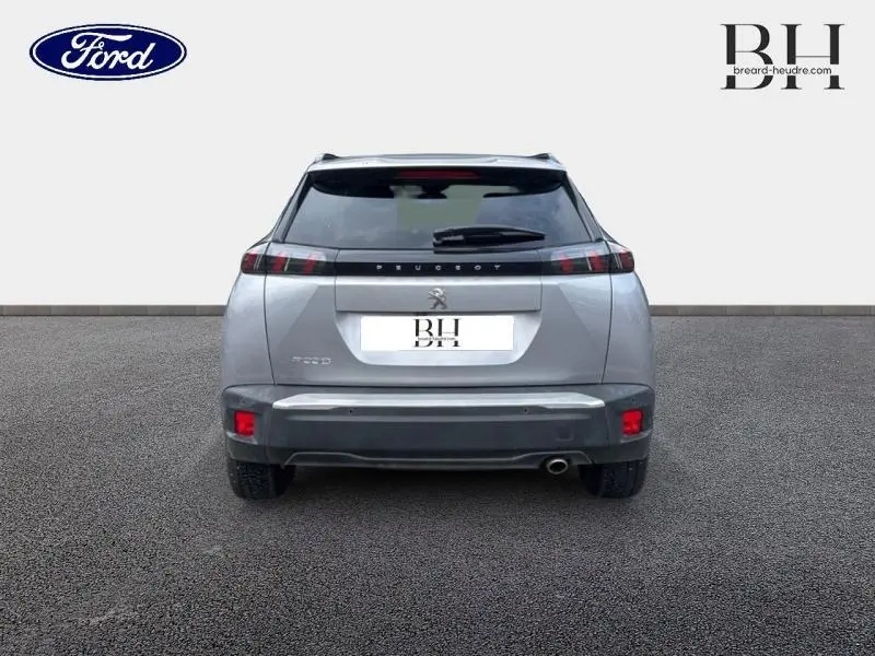 Vue arrière d'un Peugeot 2008 gris Artense avec feux arrière LED et becquet, sur sol gris neutre.