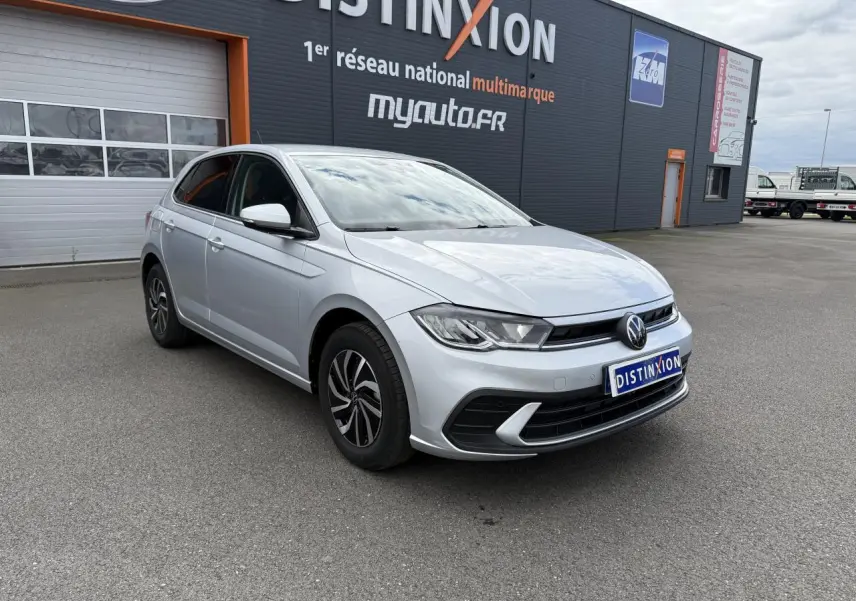Volkswagen Polo 2025 gris reflet argent vue 3/4 avant avec jantes alliage et calandre noire devant un garage.
