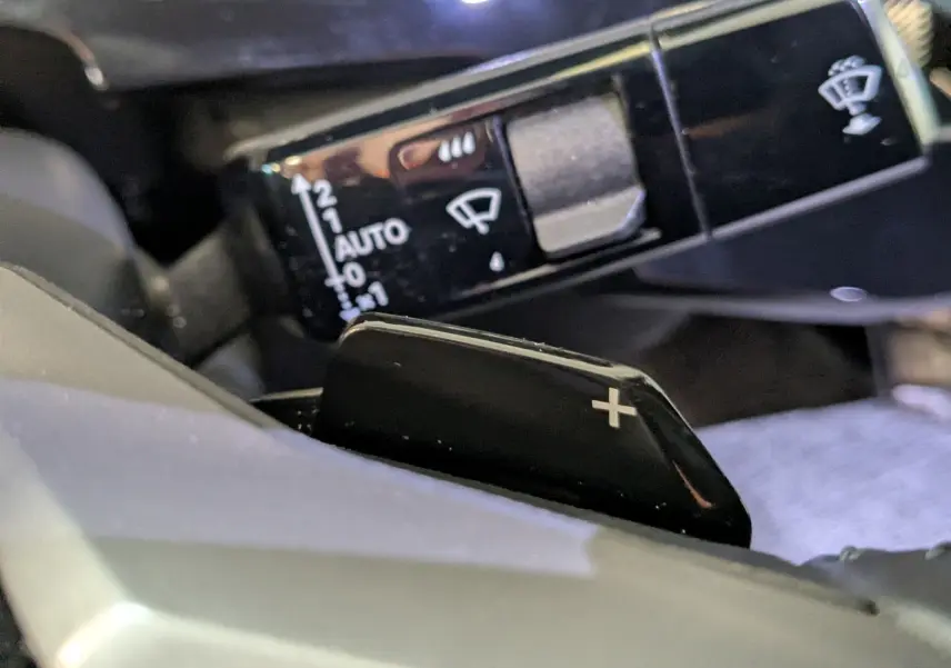 Gros plan sur la palette de changement de vitesse "+" noire et le commodo de réglage des essuie-glaces dans l’habitacle du Peugeot 3008 noir.