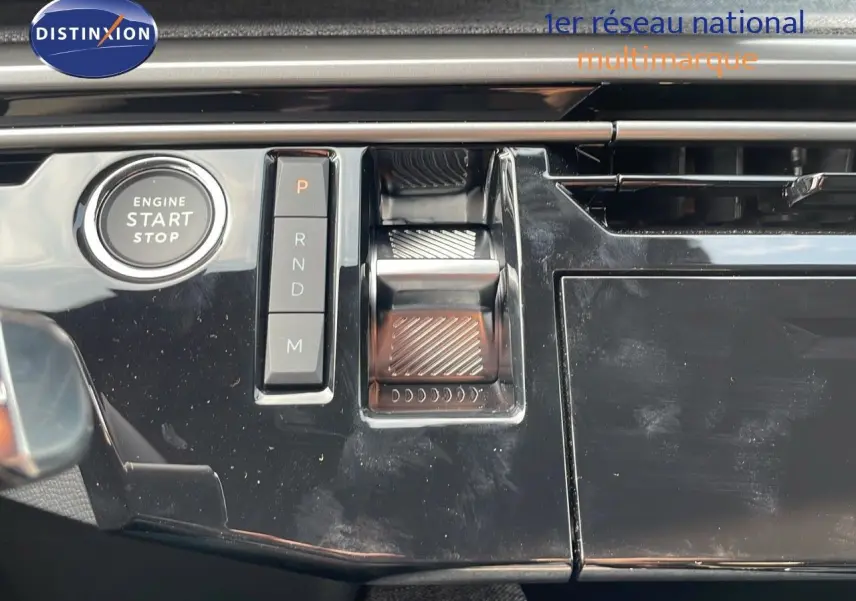 Gros plan sur la console centrale noire brillante du Peugeot 3008 Hybrid 2025 avec bouton start/stop et commandes de boîte automatique.
